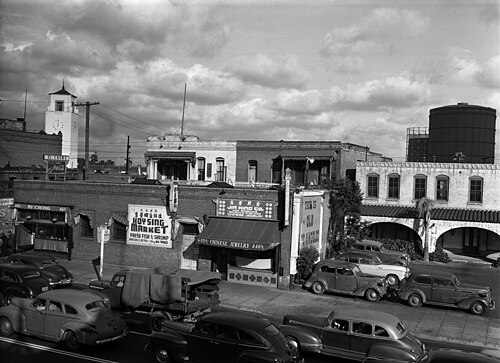 Los Angeles Street at Ferguson Alley in Old Chinatown, storefronts for a fish market and a jewelry shop, a water tower and the Union Station clock tower behind, in 1948.