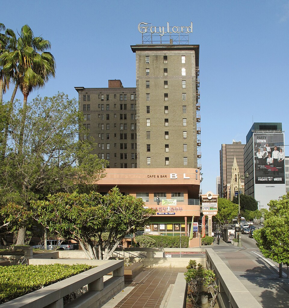The Gaylord building on Wilshire Boulevard, its rooftop sign above a ground-floor bar and cafe, a palm tree in front and a church tower visible behind it.
