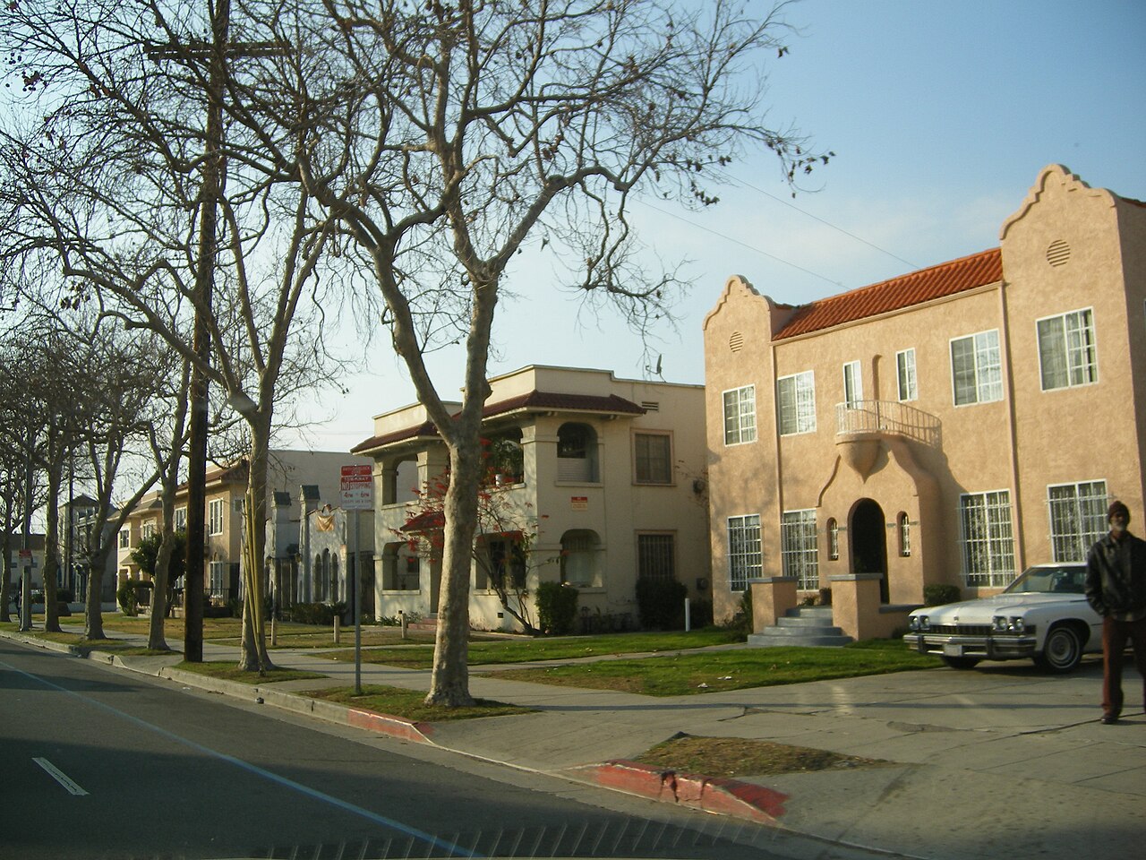 Two-story 1920s apartment buildings along Martin Luther King Jr. Boulevard, Spanish tile roofs and arched doorways, sidewalk trees and a car parked at the curb.