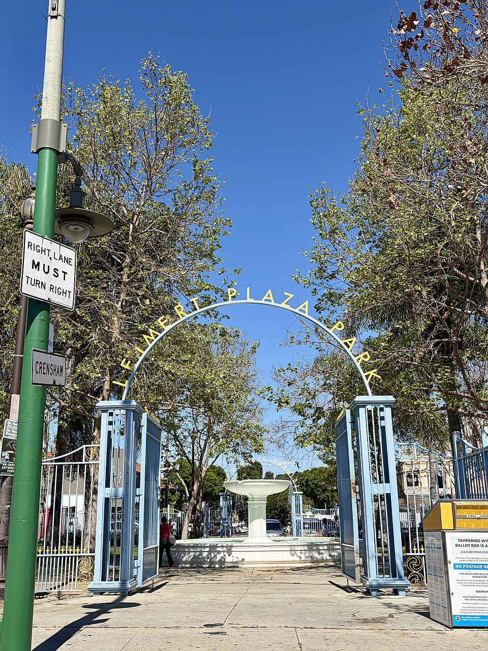 The arched gate reading Leimert Plaza Park at the Crenshaw Boulevard entrance, the park's fountain and trees behind it.