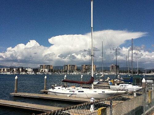 Three matching tan mid rise condominium towers across the basin, sailboat masts and a moored cruiser in the foreground dock.