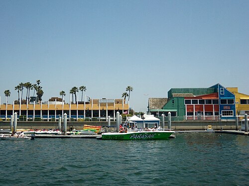 Fisherman's Village's green, red and yellow wood buildings seen from the water, a parasail tour boat docked in front.