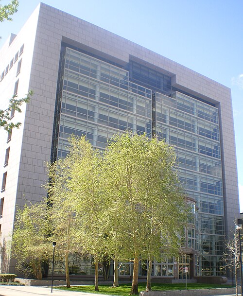 The Van Nuys Courthouse tower seen from below, a modern stone and glass building with a row of trees at its base.