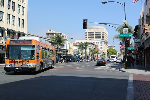 The corner of Fair Oaks Avenue and Colorado Boulevard, a Metro bus stopped at the light and historic storefronts on both sides of the crosswalk.