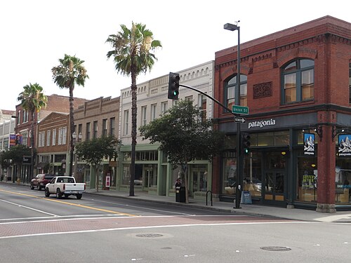 A red brick corner building at Union Street and Fair Oaks Avenue, arched cast stone storefronts along the block and palm trees at the curb.