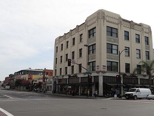 A cream terracotta corner building on Colorado Boulevard, arched ground floor storefronts and a stepped cornice with carved medallions.