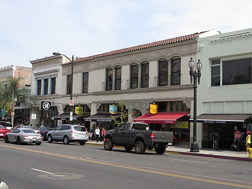 A two story Spanish style commercial block on Colorado Boulevard, a tile roof and arched upper windows over a row of restaurant and shop awnings.