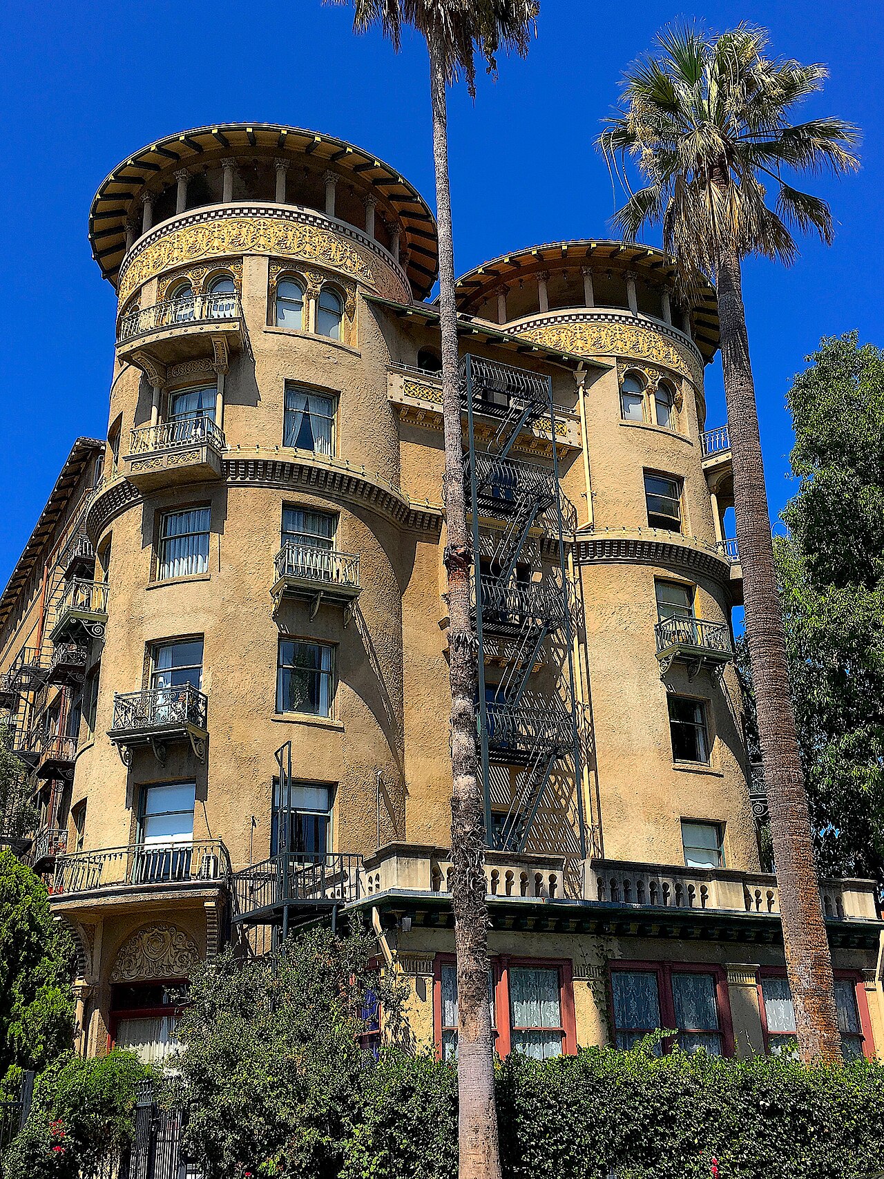 Castle Green's twin corner turrets, red tile domes over Moorish arched windows and iron fire escapes, palm trees in front.