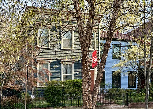 Two attached wood frame houses on D Street SE, one grey and one pale blue, behind iron front fences and young trees.