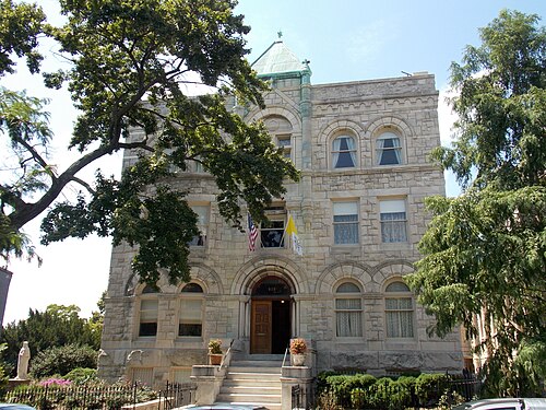 The rectory at St. Peter's Catholic Church, a steep gabled brick building with arched windows, a chimney stack and garden benches.