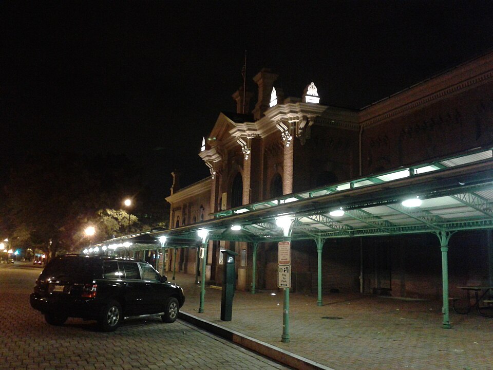 Eastern Market's brick facade and long ironwork shed along 7th Street SE, lit at night with a car parked under the canopy.