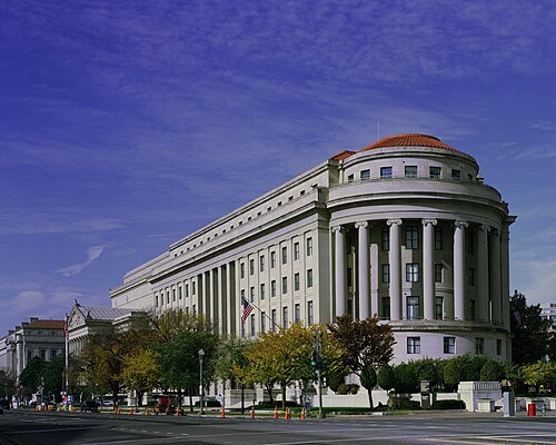 The Federal Trade Commission Building's curved colonnaded corner at dusk, columns rising the full height of the building under a red tile roof.