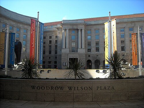 Woodrow Wilson Plaza, the Ronald Reagan Building's columned arcade hung with banners above a sunken courtyard, potted plants along the wall.