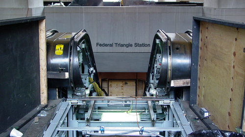The Federal Triangle station name lettered on the wall above a pair of escalators under repair, wood barriers and machinery in front.