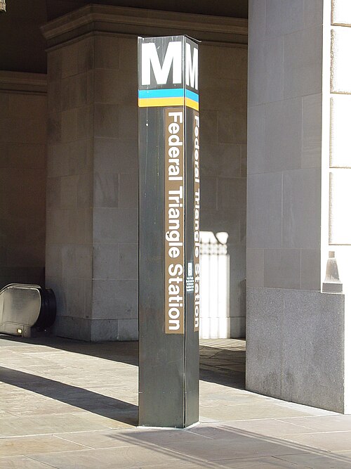 The Federal Triangle Metro station entrance pylon in front of limestone columns, an escalator visible behind it.