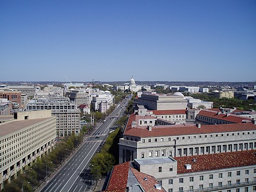 A high angle view down Pennsylvania Avenue from the Old Post Office tower, red tile roofed limestone buildings lining the avenue toward the Capitol.
