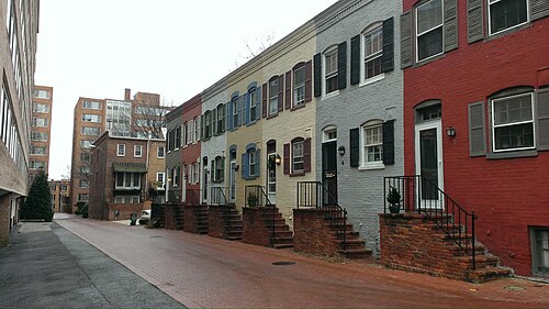 A row of two storey brick houses along Snows Court painted red, mustard, gray and blue, black iron stair rails, a taller apartment building at the end of the lane.