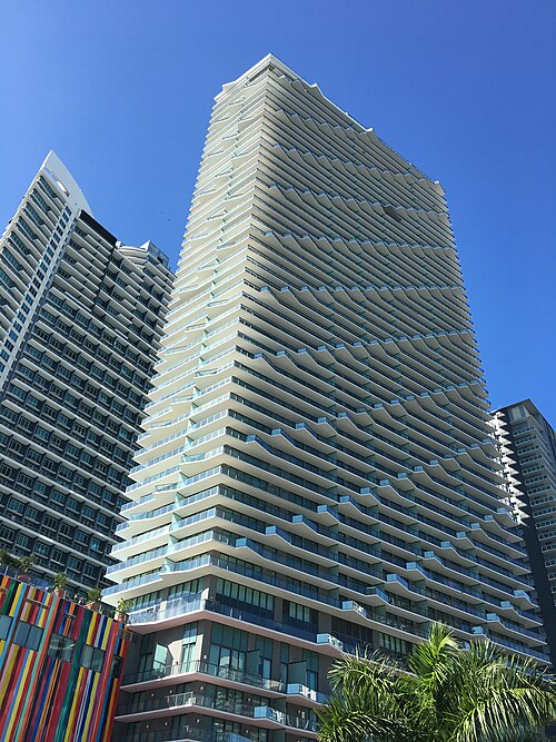 A tall tower with wavy balcony lines above a colorful striped podium building, the SLS Brickell hotel and condo tower on South Miami Avenue.