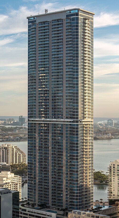 A high angle view of Panorama Tower beside the water, with lower city development around its base.