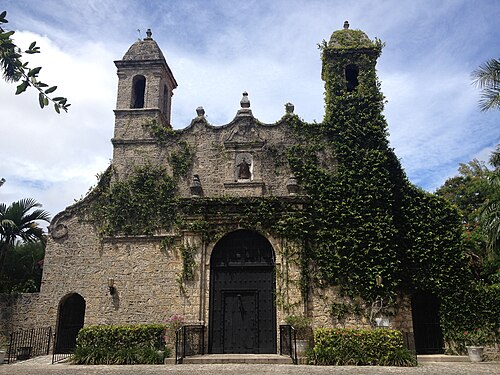 The coral rock facade of Plymouth Congregational Church, twin bell towers and an arched wooden door, ivy covering much of the stone.
