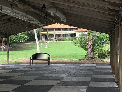 The lawn at The Barnacle running up to the Munroe House, a two storey wood frame house with wraparound porches and a red tile roof, seen from under the boat pavilion.