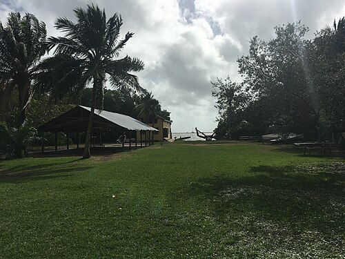 The Barnacle's open sided boathouse and lawn running down to Biscayne Bay, palm trees along the shoreline and a small boat pulled up on the grass.