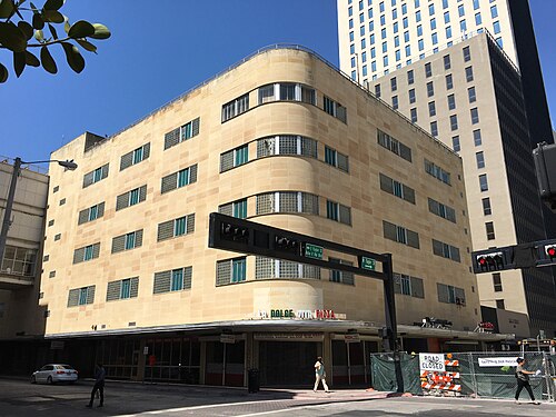 The curved Art Deco corner of the former Burdines annex on Flagler Street, cream and tan stone banding over a pizza restaurant storefront, a taller office tower rising behind.
