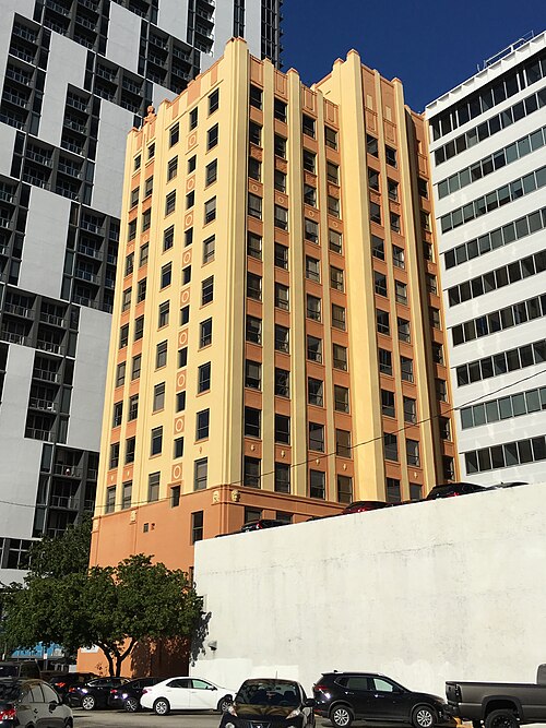 The Historic Huntington Building, a peach and orange painted Art Deco tower with vertical fluted piers, flanked by newer glass condominium towers, cars parked in a lot below.