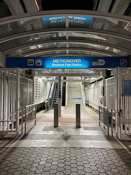 The Metromover's Bayfront Park Station entrance at night, a lit blue sign over the escalator and stairs down to the platform, gated after hours.