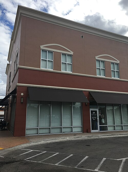 A two storey terracotta stucco corner office with arched window heads on the upper floor and dark canvas awnings over the ground floor windows.
