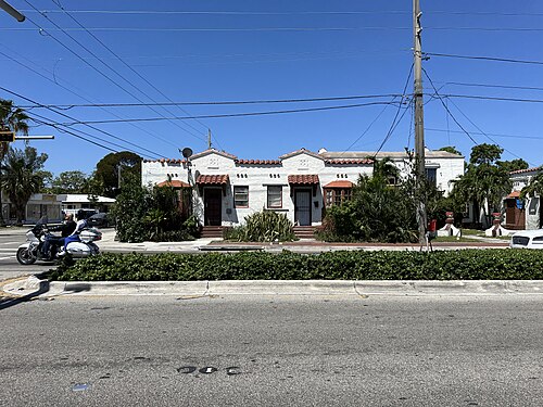 A row of Spanish Mission style apartments, red barrel tile roofs, brown arched door surrounds and white stucco walls repeating down the block.