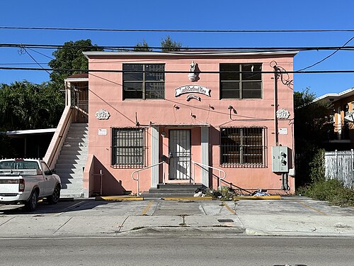 A pink two storey apartment building named Santa Barbara's House on a lettered sign above the door, a plaster medallion over the entrance and iron bars on the windows.