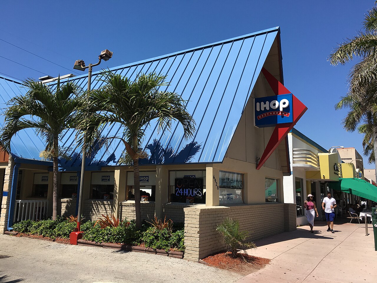 A blue folded plate roof angling up over the IHOP at 6928 Collins Avenue, palm trees against the sail shaped canopy and a red diamond sign.