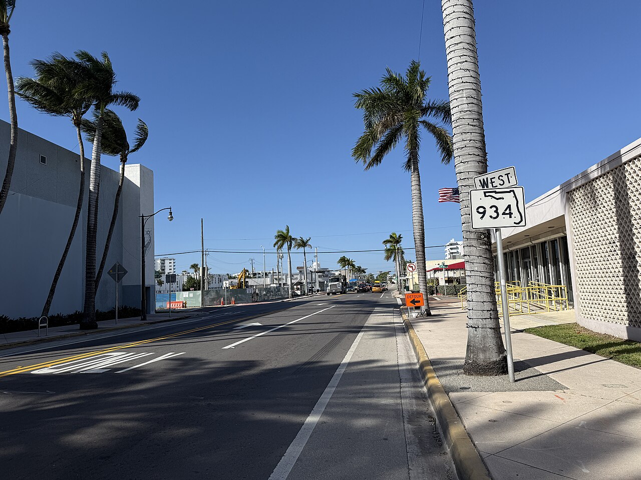 71st Street looking west, palm trees along both kerbs, a breeze block screened building on the right and a West 934 route sign.