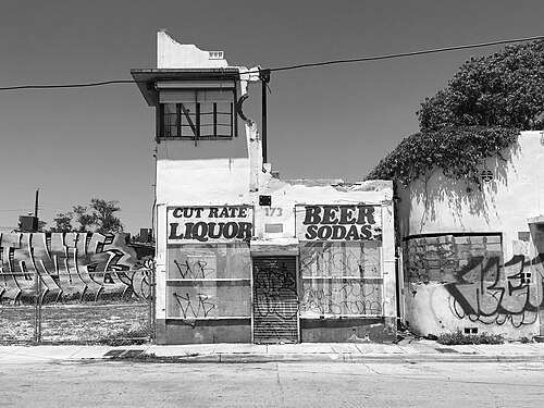 A boarded liquor store front hand painted CUT RATE LIQUOR and BEER SODAS, graffiti covering the shutters and the wall beside it.