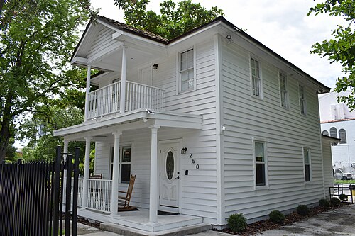 A two storey white wood frame house with a wraparound porch and an upper balcony, the number 250 over the door.