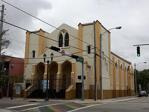 A cream and ochre stucco church on a corner, pointed gothic windows over an arched entrance porch, a traffic signal in front.