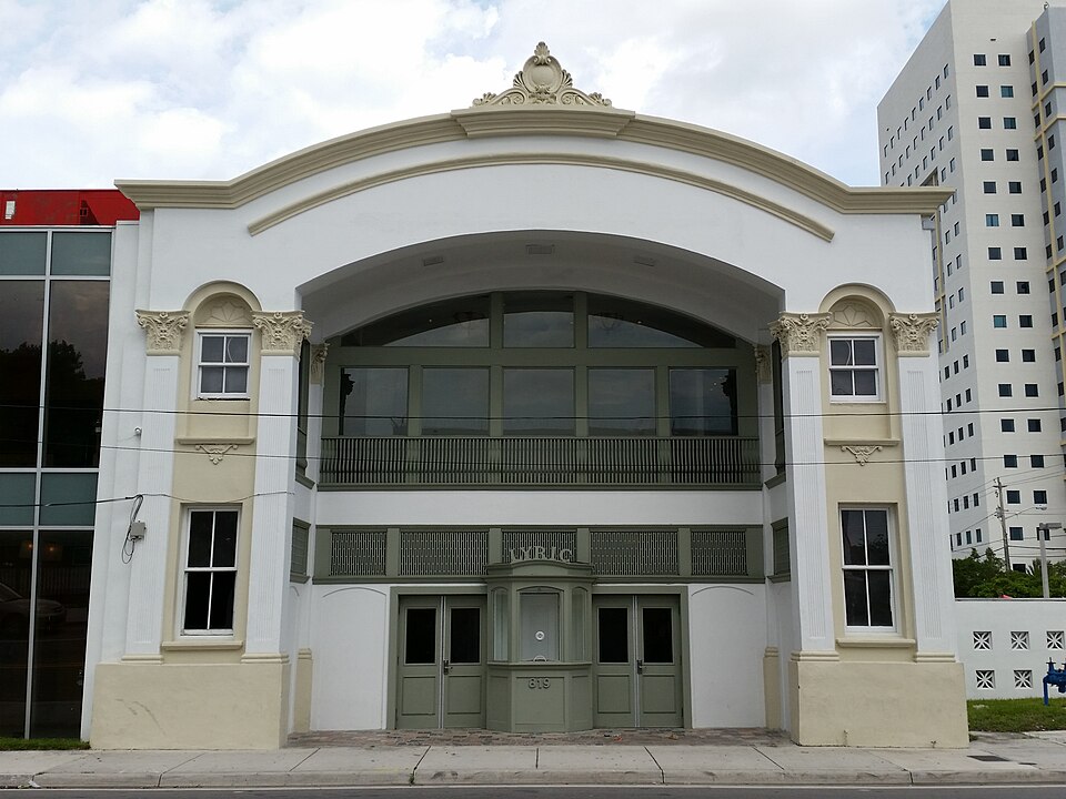 The Lyric Theater's restored front elevation in cream stucco, an arched pediment over a recessed balcony with paired columns, LYRIC lettered above the entrance doors.