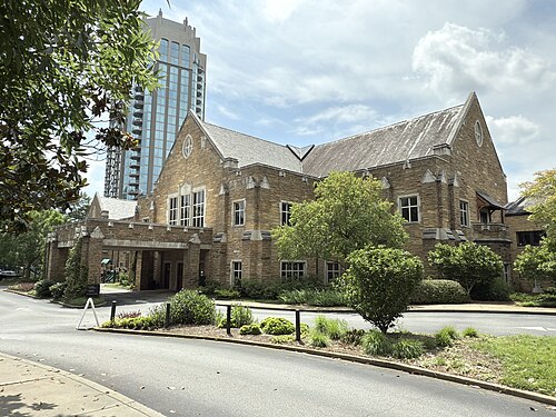 A wing of the Cathedral of St. Philip, cut stone under a steep roof, with a glass condominium tower rising directly behind it.