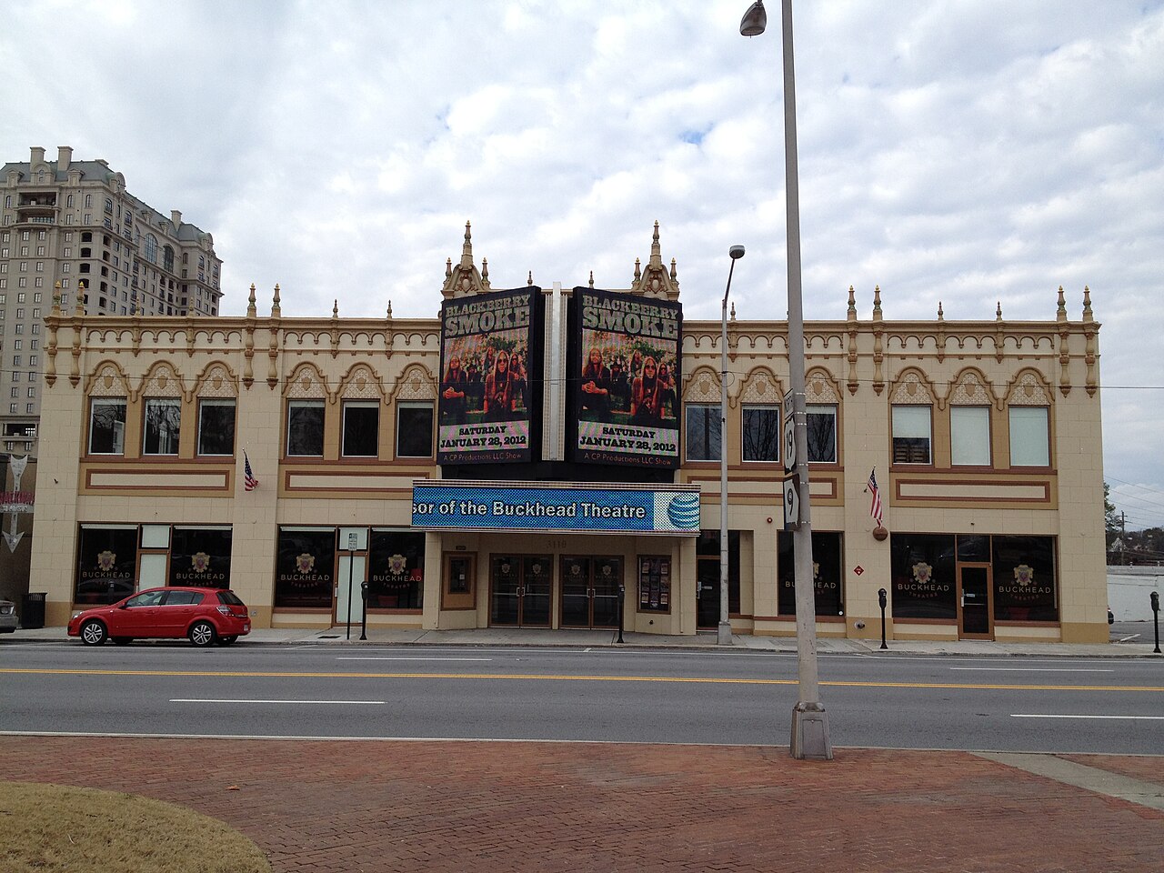 Peachtree Road at the Buckhead Theatre, a cream terra cotta movie palace with a marquee advertising a concert, a car parked at the curb and a taller building rising up the block.