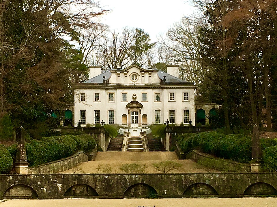 Swan House's front elevation and garden stairs, seen across the lawn between bare winter trees.