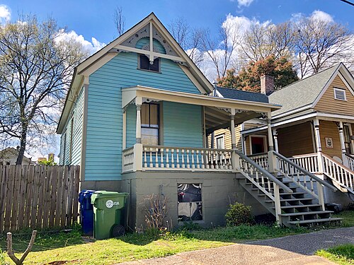 A pale blue shotgun house on Berean Avenue, a covered porch across the front and a matching cottage next door.