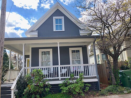 A two-story blue Victorian cottage on Savannah Street, a wraparound porch and a gabled dormer above it.