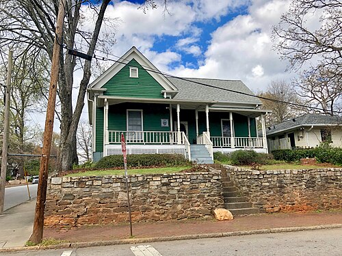 A green two-story Victorian house on Kirkwood Avenue, set above the street behind a stone retaining wall and steps.