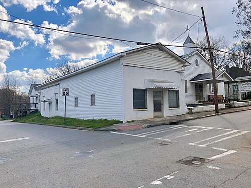 A white clapboard storefront and a small steepled building next to it at a Gaskill Street corner, seen across an empty intersection.