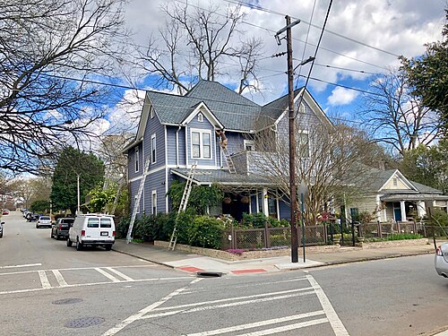 A tall blue Victorian house at a Pearl Street corner, workers on ladders along the porch and gable.