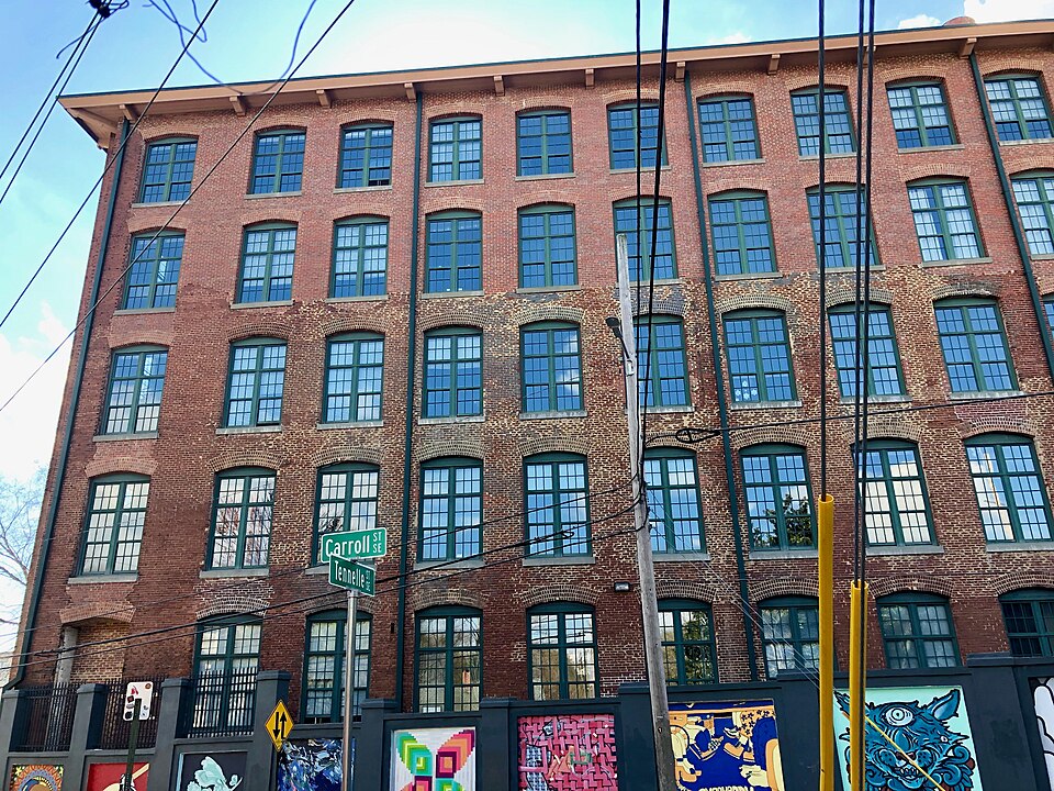 The Fulton Bag and Cotton Mill at Carroll Street, six stories of brick with arched windows on every floor, a fence covered in street art along the sidewalk out front.