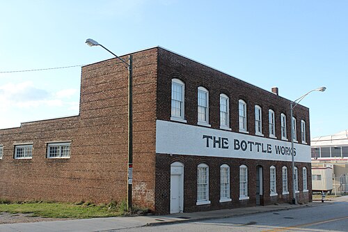A two story brick warehouse on Mangum Street with THE BOTTLE WORKS painted across its upper floor in large letters.