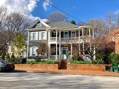 A two-story gray Victorian house on Augusta Avenue, wraparound porches on both floors, on a corner lot.