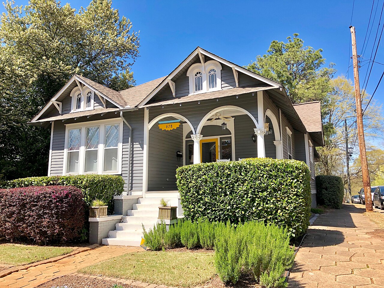 A gray craftsman bungalow on Rosalia Street, arched porch openings and a low brick and stone retaining wall along the sidewalk.